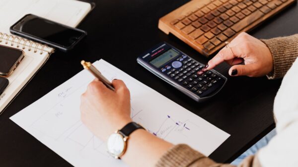 crop woman using calculator and taking notes on paper