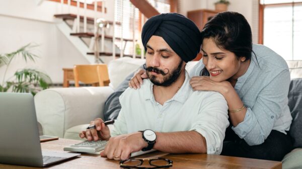 cheerful ethnic couple using calculator while sitting at table